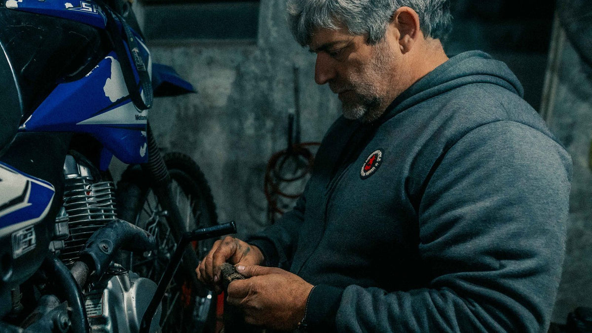 Man in a garage cleaning a greasy part beside a dirt bike