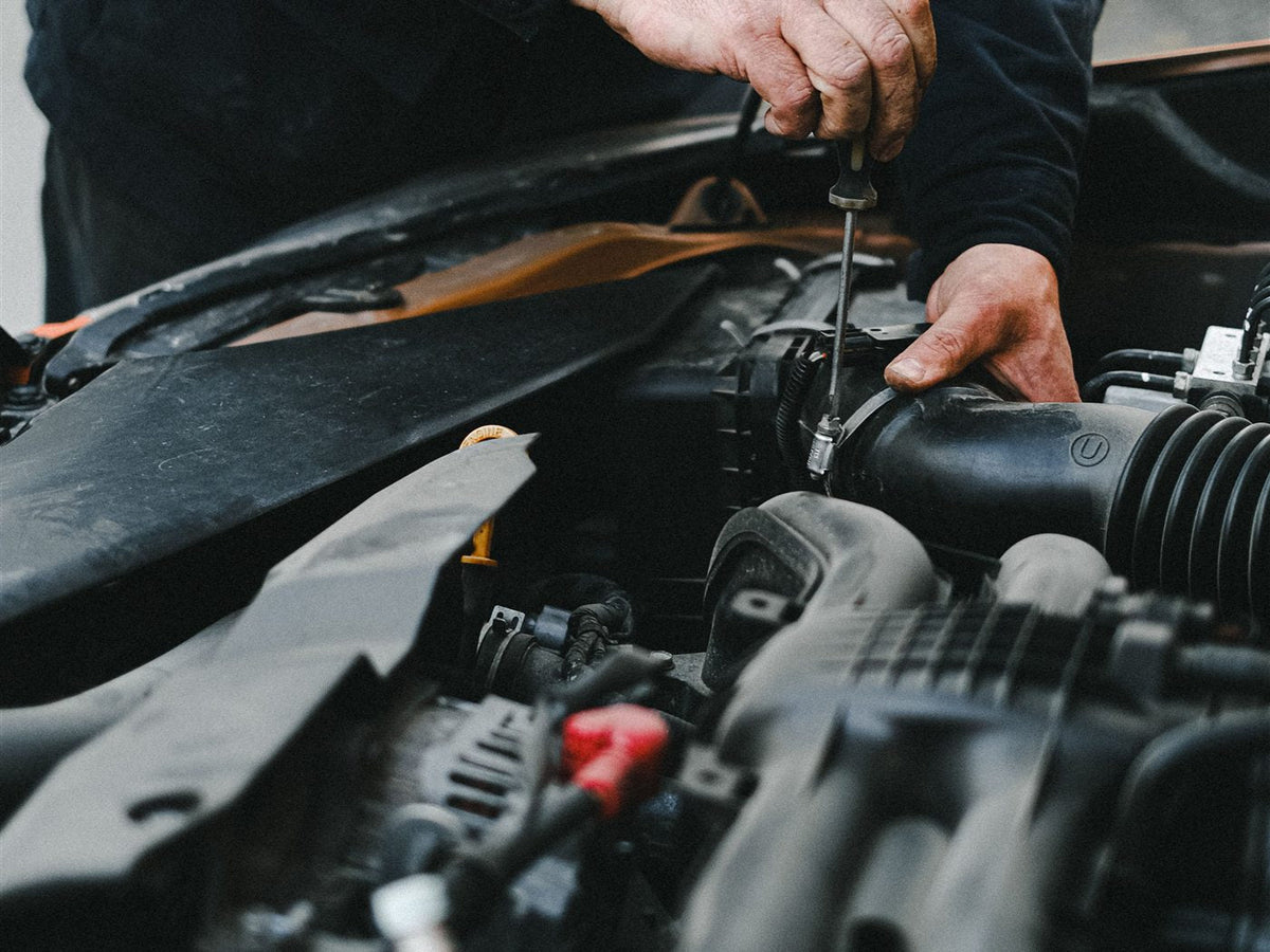 Hands loosening a hose clamp in a car engine bay with a screwdriver