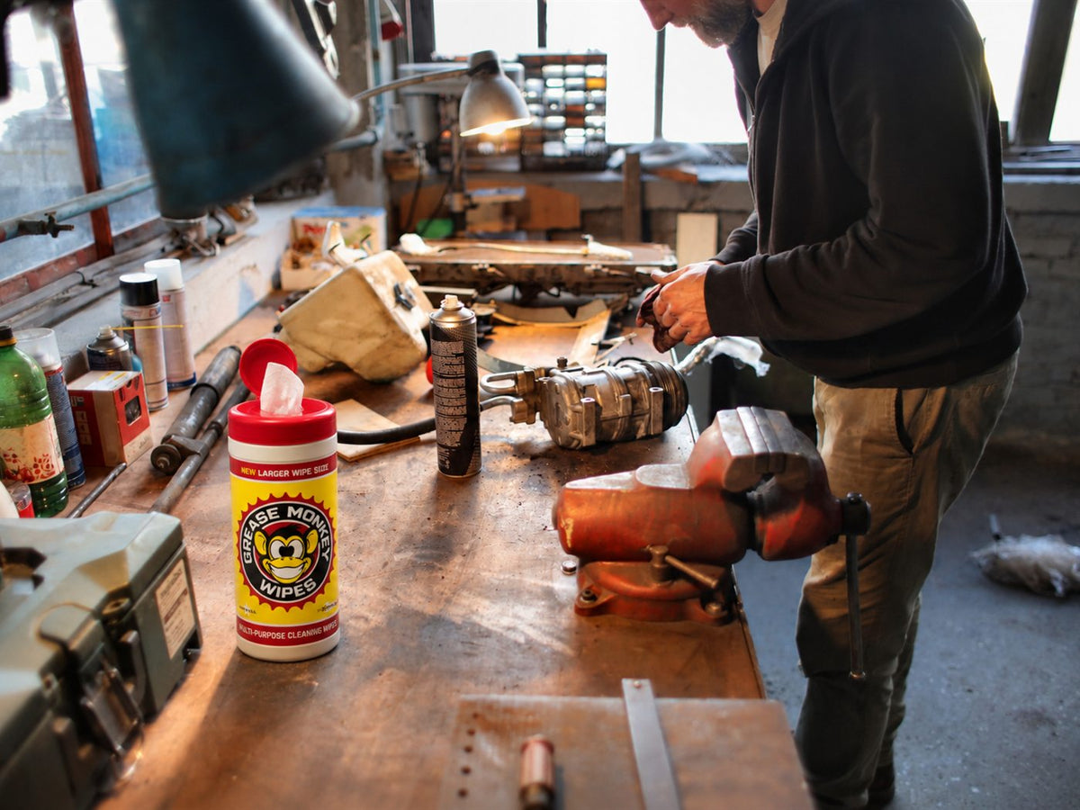 Grease Monkey Wipes canister on a workshop bench as a mechanic wipes his hands