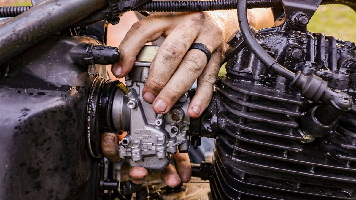 Grease-stained hands working on a motorcycle carburetor